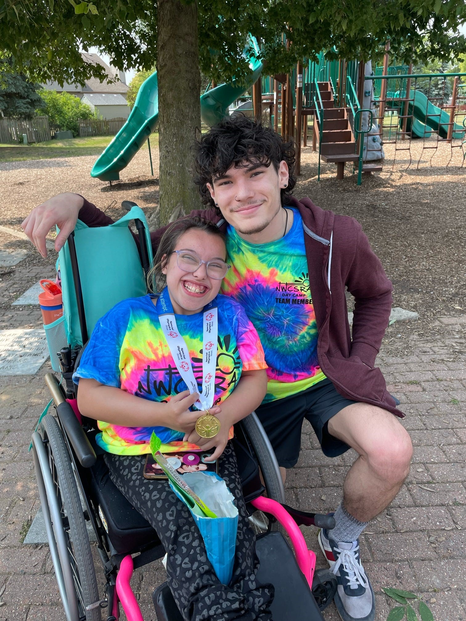 Young female summer camper with male staff member in tie dye t-shirts at outdoor playground